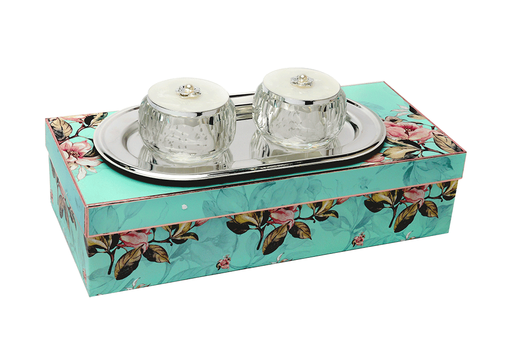 a set of two crystal bowls having enameled white lids with beads placed on a silver plated tray upon a beautiful gift box of blue floral color