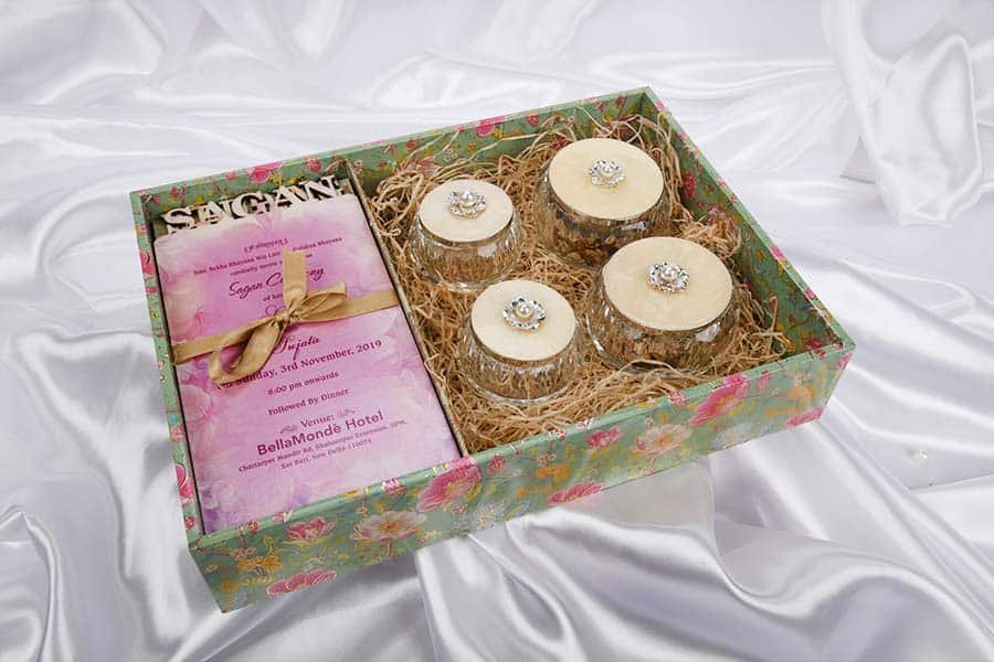 A unique & beautiful hamper including a set of four crystal bowls with enameled silver top placed inside an exclusive gift packaging box along with a wedding card on the left