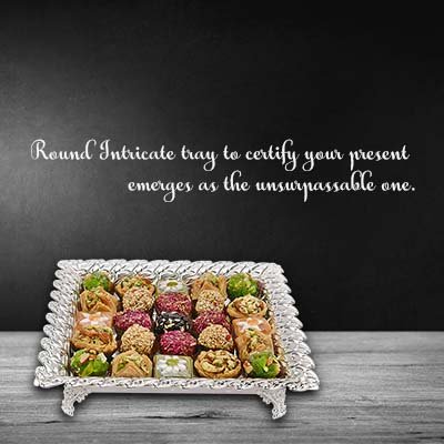 A banner of cutwork square silver tray with sweets served in it, that says," Roound Intricate tray to certify your present emerges as the unsurpassable one."