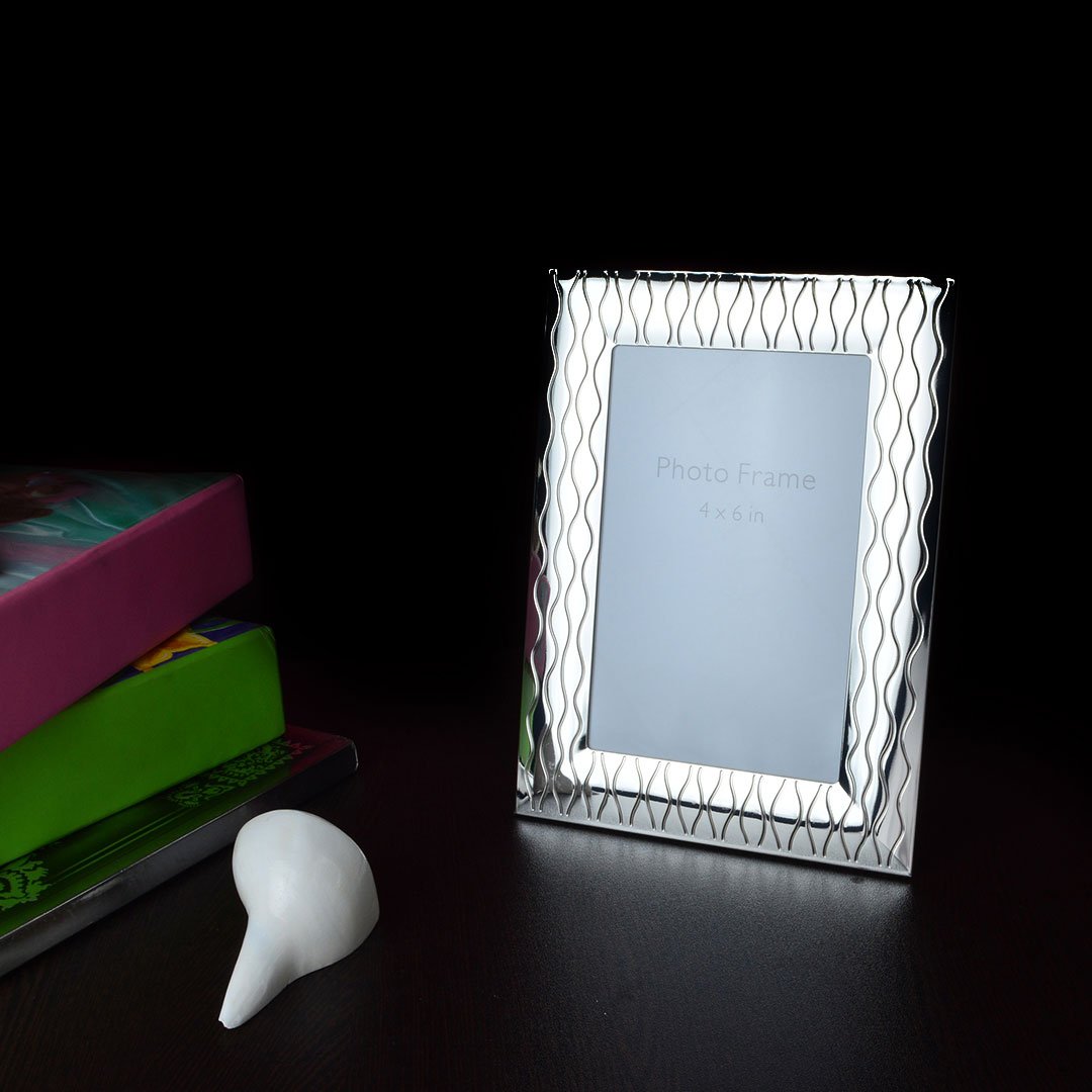 Wavy rim silver photo frame with books and conch shell on the dark surface.