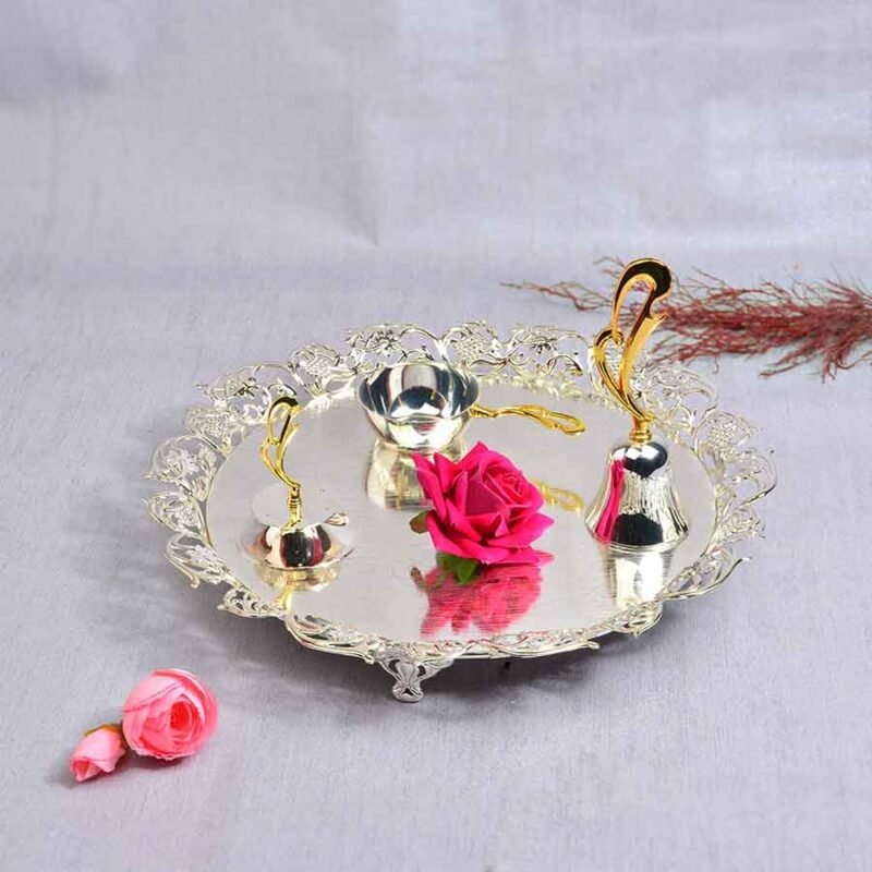 Silver Pooja Cutwork Thali Set with a silver-plated bell, Agarbatti stand and a Diya with golden handles. The background consists of artificial roses.