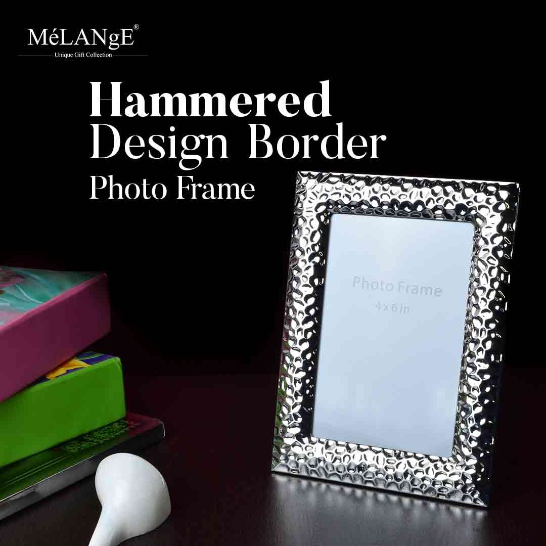 A Silver plated Hammered Design Border Photo Frame sits on a dark surface along with a few books and a conch shell.
